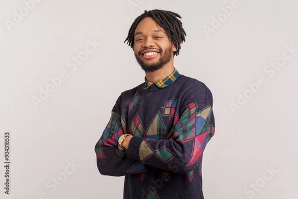 Fototapeta Portrait of handsome joyful cheerful african-american man with dreadlocks and beard standing with crossed arms and looking at camera. Indoor studio shot isolated on gray background.