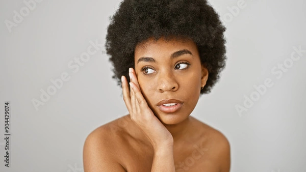 Fototapeta African american woman with curly hair touching her face, isolated on a white background, looking serene.