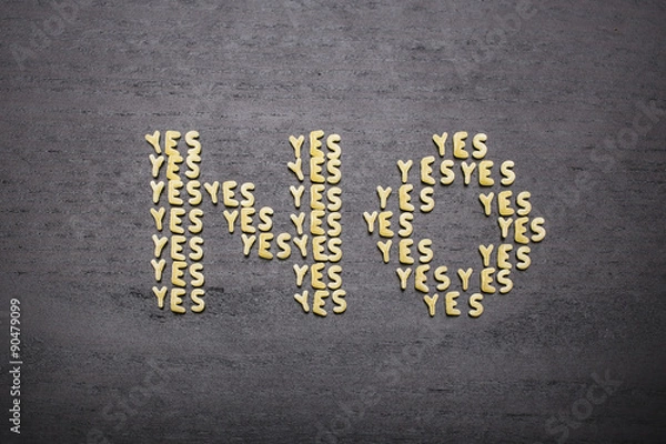 Fototapeta The answer  "no" made up of a set of words "yes", with small pasta letters on a dark background of a wooden board, showing the hidden meaning and ambiguity of the agreement.