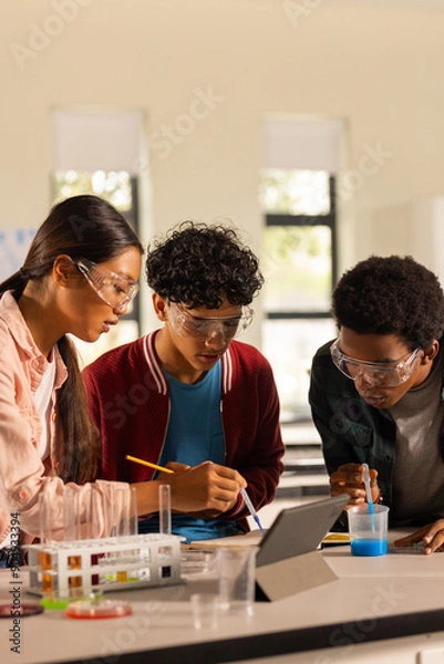 Fototapeta Conducting science experiment, teenagers using tablet and lab equipment in high school