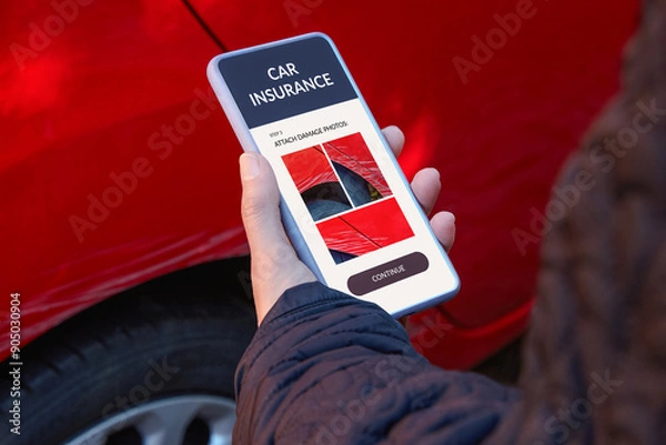Fototapeta Reporting car damage through mobile technology. Woman standing by her car, holding a smartphone and sending photos of scratches on the vehicle for insurance purposes.