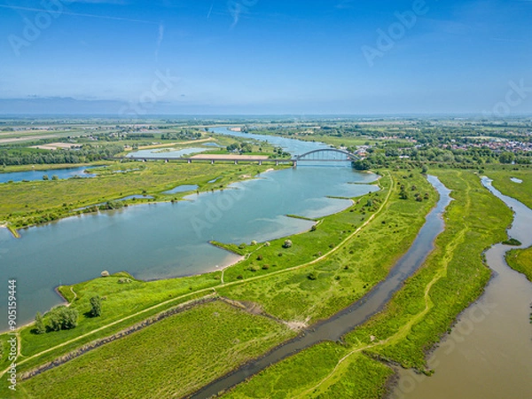 Fototapeta Aerial photo of a hiking trail through the flood plains along the Lek River with the Kuilenburgse train bridge crossing the river near Culemborg.