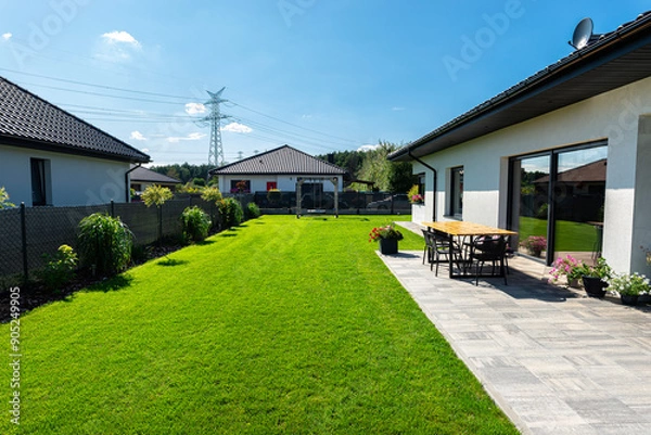 Obraz Beautiful garden with green grass, visible terrace table and house in beautiful summer weather, very wide shot.