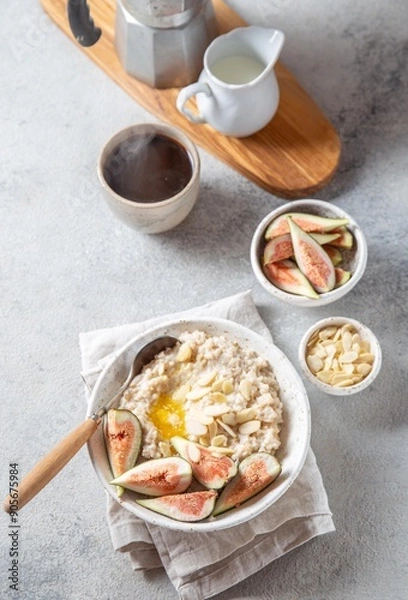 Fototapeta A wholesome bowl of oatmeal topped with fresh figs and sliced almonds, set on a rustic linen cloth. Accompanying small bowls of figs and almonds enhance the cozy breakfast scene