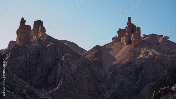Fototapeta The rugged beauty of a desert landscape is captured as the sun casts its glow on sandstone spires, which stand proudly against a clear, pale sky.