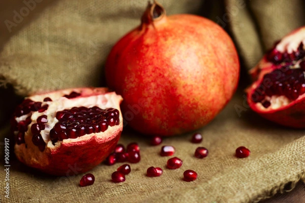 Fototapeta Raw red bright pomegranate with seeds on sacking background