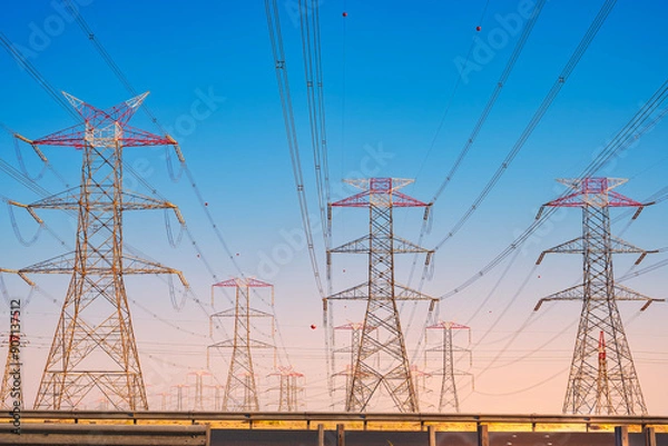 Fototapeta Overhead line pylons, high voltage pylons. Power transmission towers and lines at sunset. A shot of high voltage electric transmission tower, also known as electricity pylon...