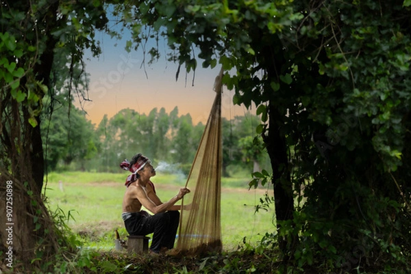 Fototapeta Asian fisherman sitting on wooden chair smoking and checking net before catching freshwater fish in nature river at the countryside.Life style and rural life concept.