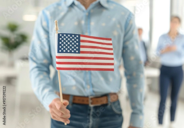 Obraz Close up of an American flag being held in the style of one person in the foreground, blurred people holding US flags and dressed in business casual standing behind him in a blurry background.