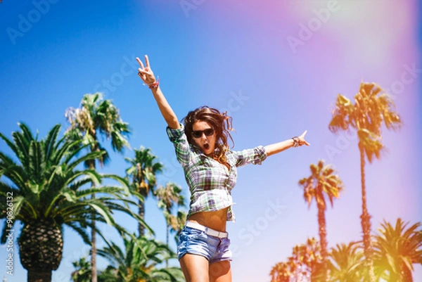 Fototapeta Beautiful young crazy happy girl is jumping in palm trees in summer in Barcelona