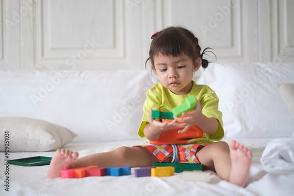 Fototapeta Young child playing with colorful building blocks on bed, developing skills and having fun in a bright room.
