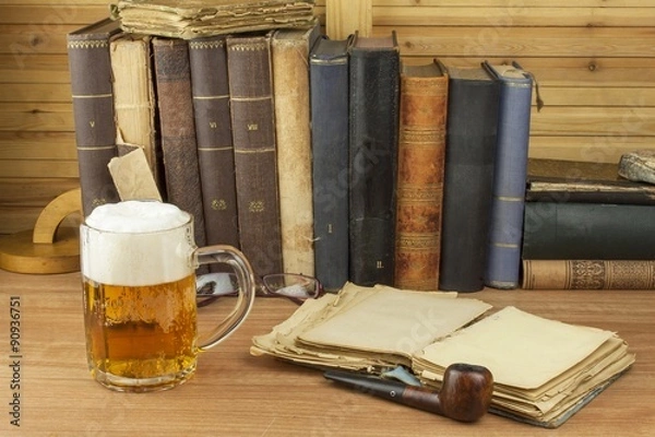 Fototapeta Cool glass of beer on the table. Relax with a good book with a glass of cold beer. The concept relax with a good beer. Pouring a glass of beer for readers of the book. Alcohol and study.
