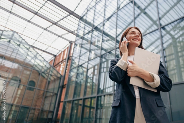 Fototapeta Confident Businesswoman talking on the phone while holding documents in a modern office setting