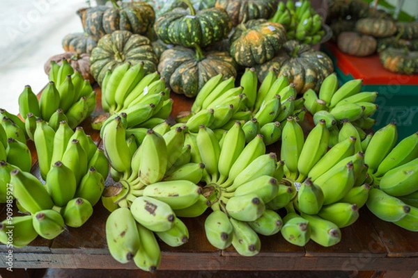 Obraz Raw bananas in green color and pumpkins put on merchandise shelf for selling.