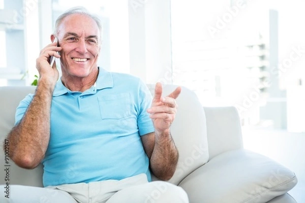 Obraz Senior happy man using smartphone while sitting on sofa