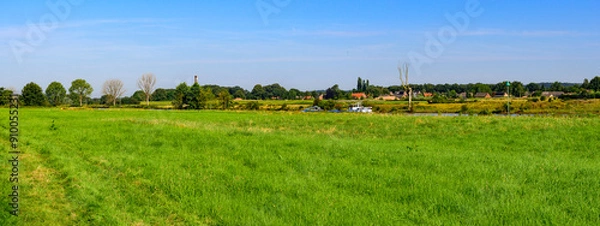 Fototapeta Panorama photo mid summer of a landscape at the edge of the river "De Maas" Noord Brabant, Netherlands. Surrounded by green nature and a clear blue sky.