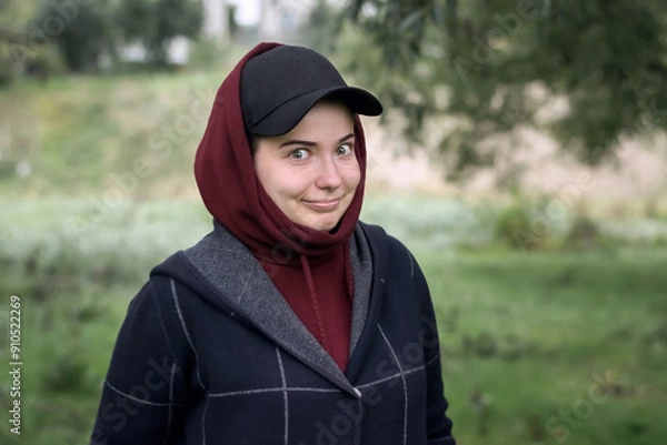 Fototapeta A funny girl in a cap and hood with smile in nature