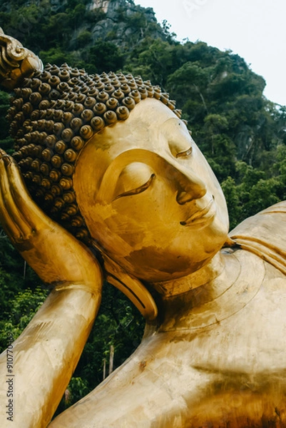 Fototapeta Vertical image of huge gold Reclining Buddha statue with mountain background inThailand.