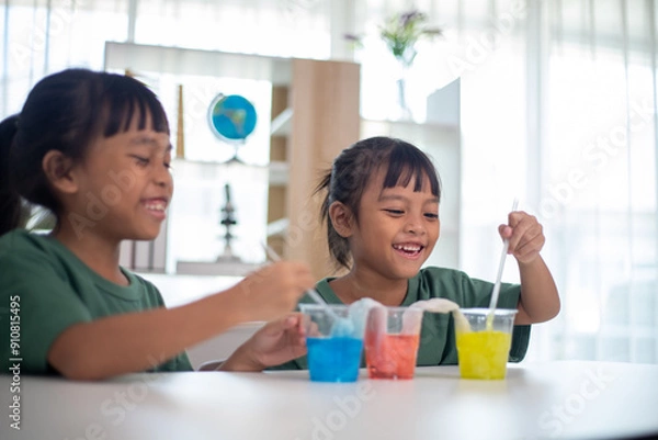 Fototapeta Two young girls are sitting at a table, playing with a science experiment