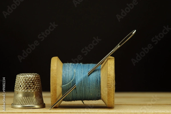 Fototapeta Old spool of thread with needle closeup. Tailor's work table. textile or fine cloth making.