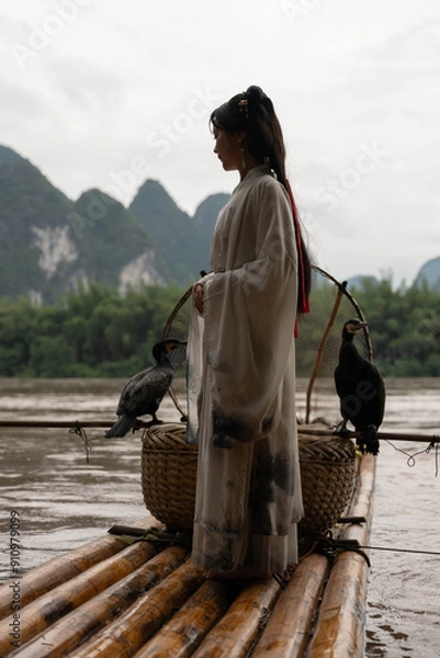 Obraz Chinese Hanfu girl fixing her hair while standing on bamboo raft by Li river, Xingping