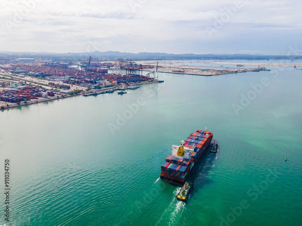 Fototapeta the aerial perspective of a cargo ship being loaded and unloaded at a bustling seaport and sailing out of the mainland