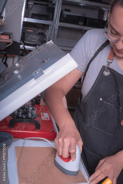 Fototapeta Working woman in her workshop doing the sublimation process with a heat press.