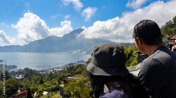 Fototapeta Back view of a tourist couple looking at Batur Lake and Trunyan Hill in Bali. The couple enjoys the scenic view, highlighting the natural beauty of the landscape. Travel and nature photograpy concept