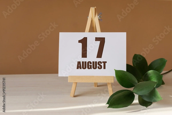 Fototapeta August 17th. Day 17 of month, Calendar date. Green branch, easel with the date and month on desktop. Close-up, brown background. Summer month, day of year concept