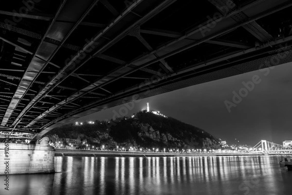Obraz A stunning night view of Budapest featuring the illuminated Chain Bridge and Gellért Hill, with the Danube River reflecting the city’s lights.