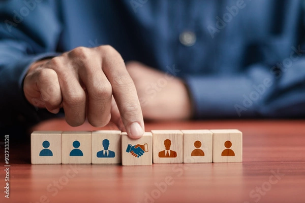 Fototapeta Businessman arranging wooden blocks with handshake icon and people icon for business joint venture concept. data exchange customer connection, teamwork and successful business.