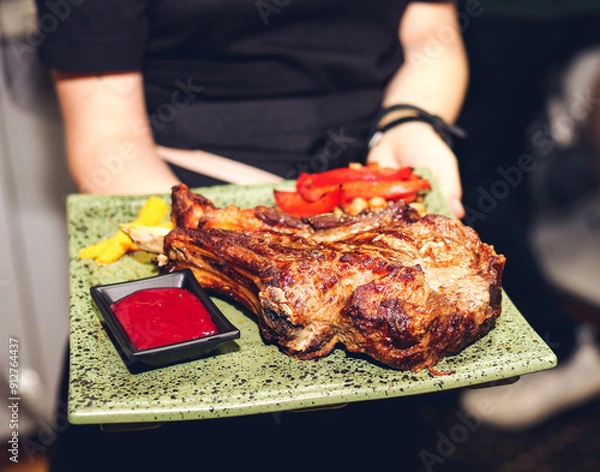 Fototapeta Waiter carrying grilled rib on stone tray with beautiful serving