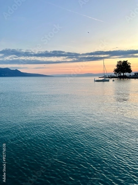 Obraz Sunset over calm waters in Lake Geneva. taken in Vevey Switzerland.  Sailboat in the water and the Swiss alps in the background.  No people.
