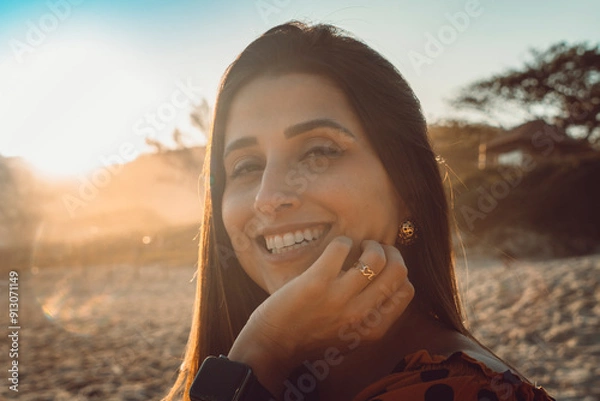 Fototapeta Beautiful brunette girl headshot close-up on a beautiful smiley face on a beach with sun rays coming in by sunset
