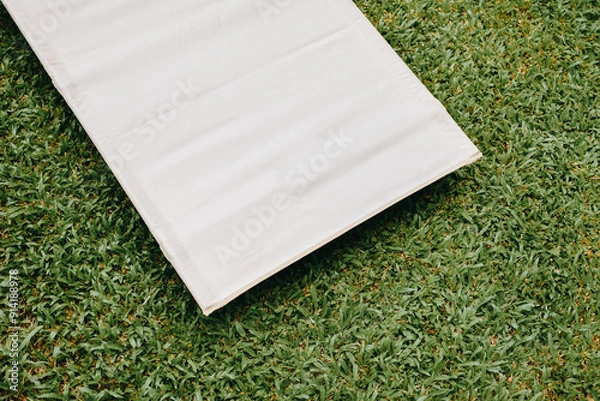 Fototapeta White camping bed or cot for camping or travel on green grass background. Copy space.