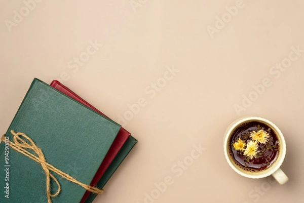 Fototapeta Stack of books with cup of herbal tea on a beige background. Leisure concept, reading a book. Copy space. Flat lay, top view