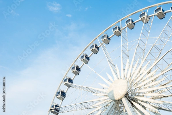 Fototapeta A large ferris wheel in an amusement park under a partly cloudy sky, offering panoramic views and thrilling rides for visitors.