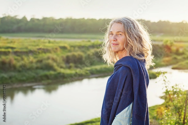 Obraz Beautiful mature woman standing in front of the river in autumn