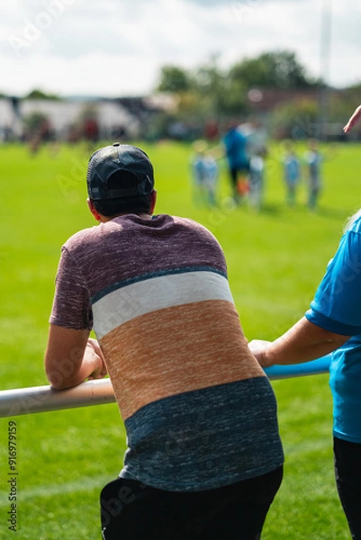 Obraz Viewer of a Football Game Standing on the Sideline Watching the Soccer Players Play on the Green Field