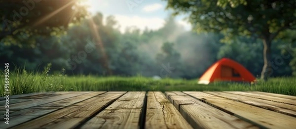 Fototapeta Blurry camping tent with grass field background featuring a wooden table top Ideal for product display or design layouts with a fresh and relaxing theme including copy space images