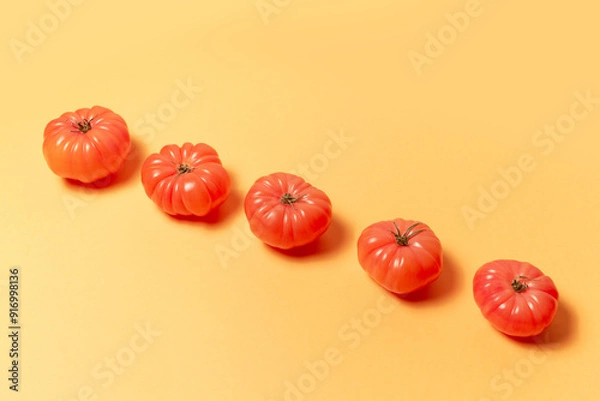 Fototapeta Close-up of pink tomatoes on background of pastel yellow color. Top view. Colourful pattern.