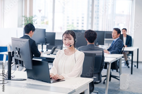 Fototapeta ヘッドセットをつけて話す若いビジネスウーマン