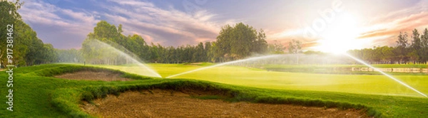 Fototapeta Golf course sprinklers in action at sunset. Concept of maintaining a lush green fairway