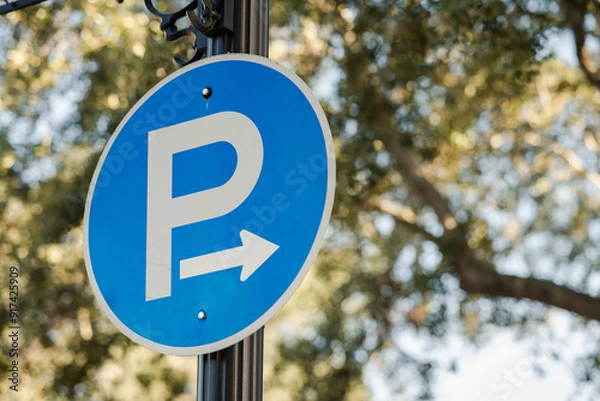 Obraz Round blue P for Parking sign with arrow, trees and sky in background