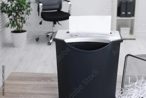 Fototapeta Destroying sheets of paper with shredder on wooden table in office