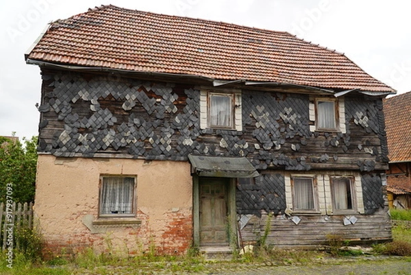 Fototapeta Facade of an abandoned house made of wood with panels of natural slate, most of the slates have fallen off. Background image of a lost place. Elende Bleicherode, Nordhausen, Thuringia, Germany.