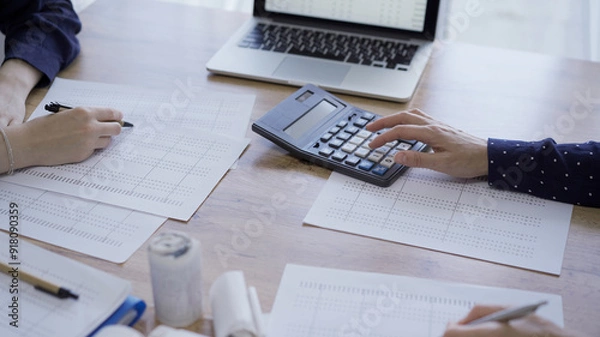 Fototapeta Accountants or auditors reviewing financial documents while using laptop, calculator and sitting opposite one another at the wooden desk in office, view above. Audit and taxes