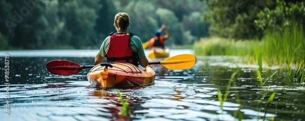 Fototapeta Two kayakers enjoying a peaceful paddle on a serene lake surrounded by lush greenery and tranquil waters.