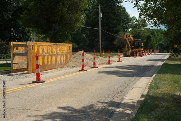 Fototapeta A trench box and excavator for water line replacement work on a city street with traffic cones for lane closure