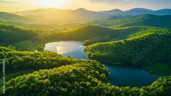 Fototapeta "A beautiful landscape of green mountains and a lake in the morning with a sunrise sky. This nature scene showcases a watershed forest, highlighting water and forest sustainability. The aerial view re